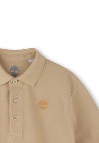 Beige polo shirt met een drieknops sluiting, geribde kraag en geborduurd logo op de linkerkant van de borst. Gestructureerde stof met een subtiel patroon.