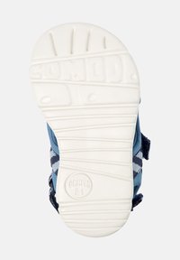 Vit texturerad sula med "Camper 21"-logotyp, fäst vid blå och marinrandiga sandalremmar synliga från sidan.