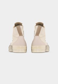 Ζευγάρι από εκρού ψηλά sneakers με μπεζ επιθέματα στη φτέρνα και χοντρές καουτσούκ σόλες, εμφανιζόμενα από πίσω σε λευκό φόντο.