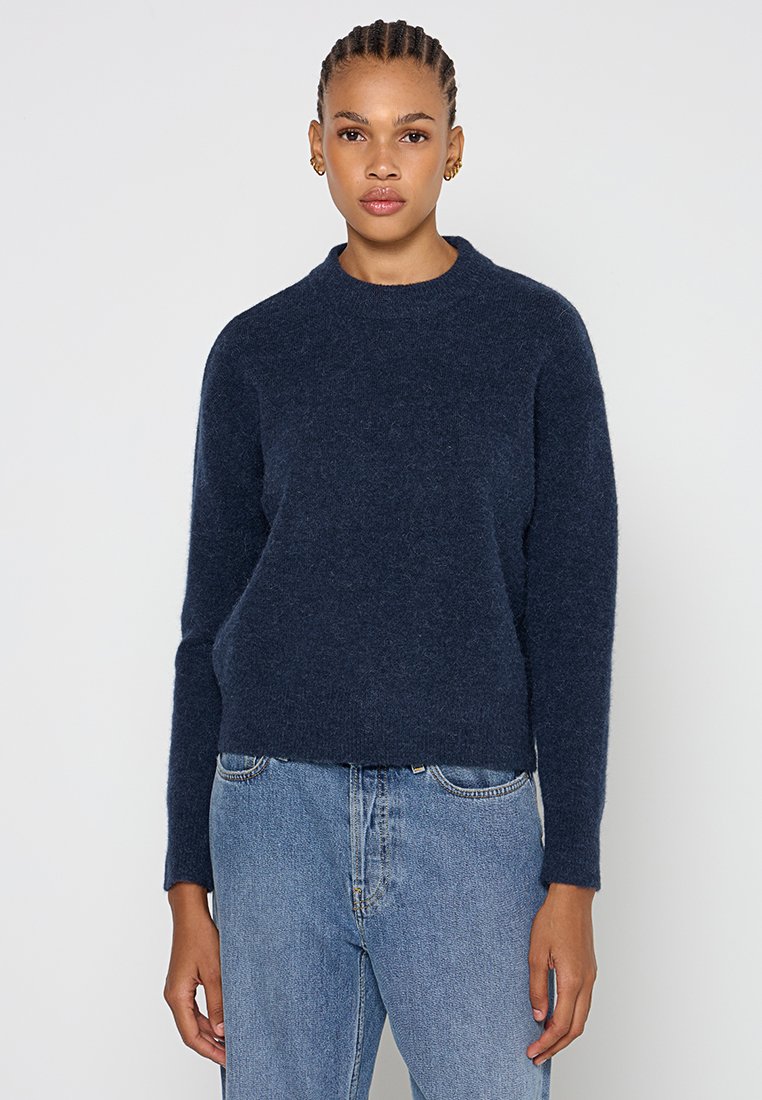 Marineblauer, flauschiger Strickpullover mit Rundhalsausschnitt und langen Ärmeln, kombiniert mit hellblauen Jeans. Minimalistisches, lässiges Design.
