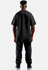 Zwart oversized T-shirt met een losse pasvorm, korte mouwen en een gladde textuur, gecombineerd met bijpassende zwarte taps toelopende broeken en sneakers.