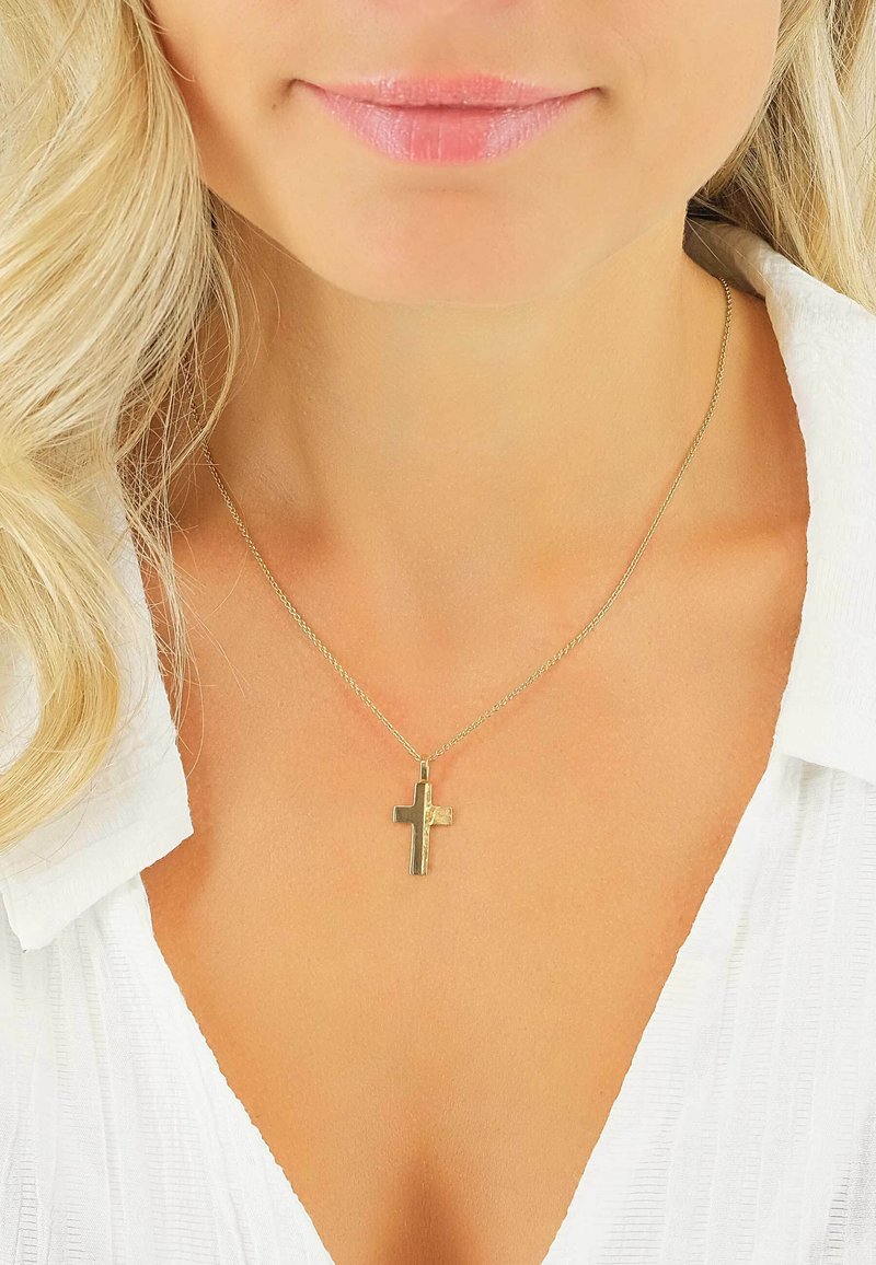 Gros plan sur le cou et la poitrine d'une femme portant un pendentif croix en or sur une fine chaîne avec un col de chemise blanche visible.