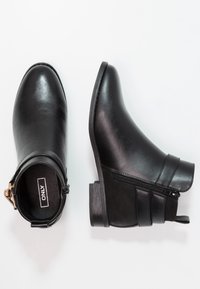 Černé kotníkové boty vyrobené z hladké kůže s nízkým blokovým podpatkem, bočním zipem a dekorativními pásky. Interiér obsahuje značka.