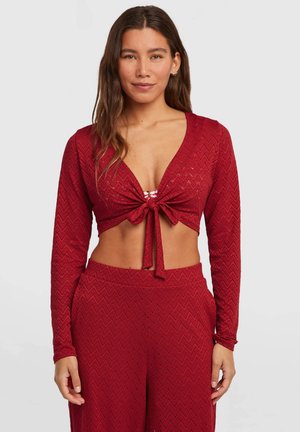 Top rosso corto con maniche lunghe, scollo a V e nodo frontale. Presenta un motivo a zigzag e un tessuto lavorato. Abbinato a pantaloni a vita alta coordinati.