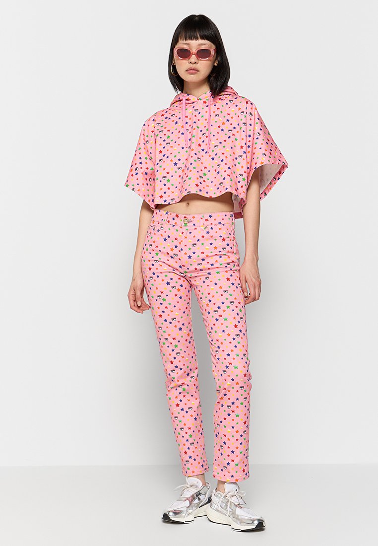 Ensemble rose assorti composé d'un hoodie court et d'un pantalon slim, tous deux ornés de motifs d'étoiles multicolores. Le mannequin porte des baskets réfléchissantes et des lunettes de soleil.