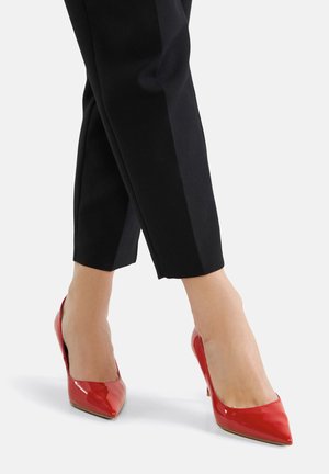 Rote Lackleder-Pumps mit spitz zulaufender Spitze und schlankem Absatz, kombiniert mit maßgeschneiderten schwarzen, knöchellangen Hosen.