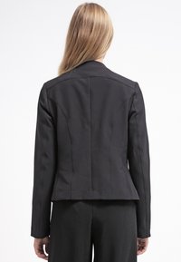 Blazer noir cintré avec des épaules structurées, une taille ajustée et une texture de tissu lisse. Présente des coutures précises et un design élégant.