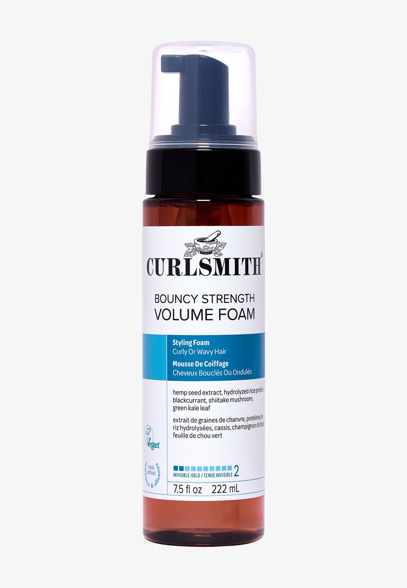 La mousse volumisante Bouncy Strength de Curlsmith dans un flacon pompe transparent, rempli de liquide ambré, présente une étiquette blanche et bleue avec des détails sur les ingrédients.