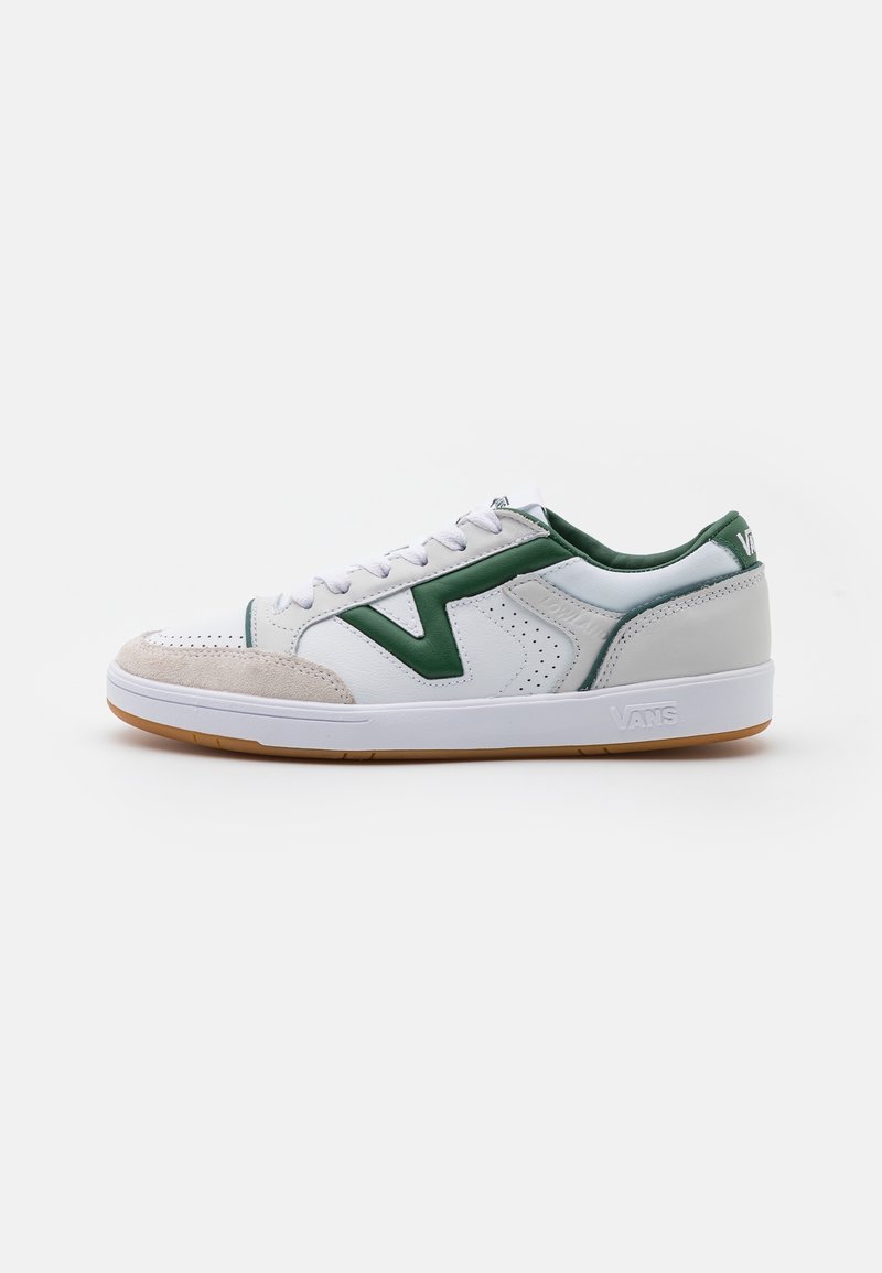 Baskets basses Vans en cuir blanc avec des touches vertes sur le logo et un bout en daim beige sur une semelle en gomme, vue latérale.