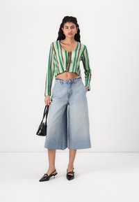 Zöld zigzag mintás crop top, világoskék, magas derekú, bő szárú farmernadrág, fekete kézitáska és hegyes orrú fekete magassarkú cipő.