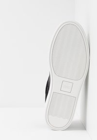 Sneaker nera con tomaia texture, suola in gomma bianca e logo del marchio impresso sul tallone. Presenta un motivo a battistrada ondulato per una migliore aderenza.