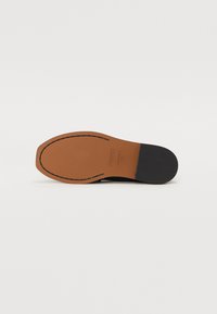 Semelle de chaussure noire avec cuir tan, présentant une pointe arrondie et une texture lisse. Des coutures visibles le long du bord ajoutent du détail.