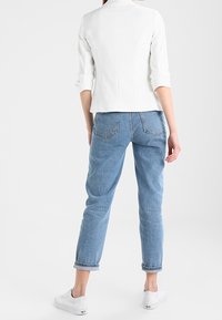 Witte getailleerde jas met opgerolde mouwen, gecombineerd met lichtblauwe relaxte spijkerbroek en witte sneakers; gladde stof en klassiek ontwerp.