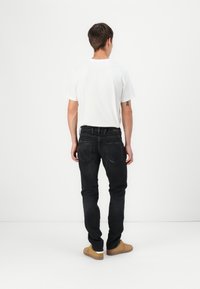 Jeans in denim nero con una vestibilità slim, design a cinque tasche e dettagli di cucitura sottili, abbinati a una t-shirt bianca semplice e scarpe beige.