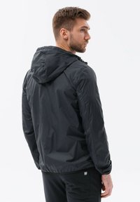 Sort hættetrøje lavet af let materiale. Designet med en glat tekstur og elastiske manchetter, har den en sammensnærpet kant for en sikker pasform.