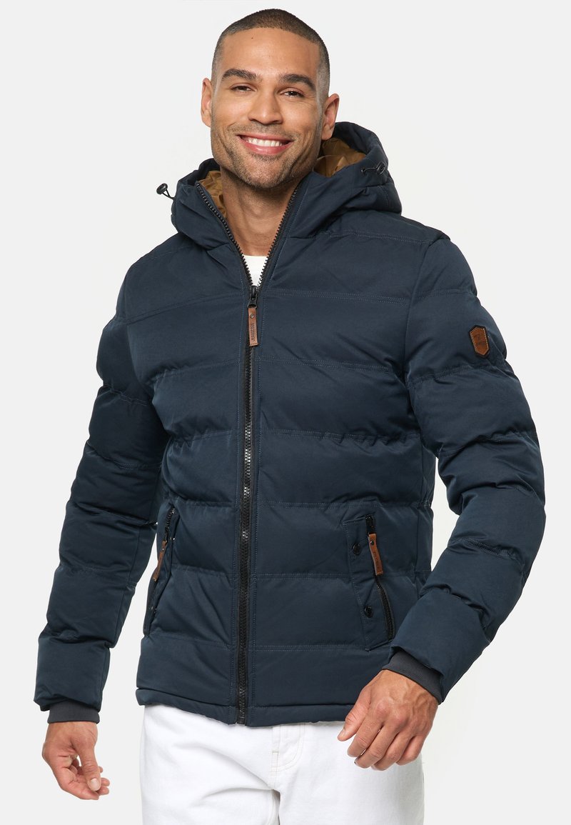 Marineblauer Puffermantel mit abnehmbarer Kapuze, Reißverschluss vorne, Akzenten aus Kunstleder und zwei Seitentaschen; gestepptes Design und verstellbare Bündchen.