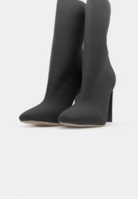 Stivaletti neri con tacco kitten realizzati in tessuto morbido, con punta affusolata e design senza cuciture, dotati di un alto tacco a stiletto.