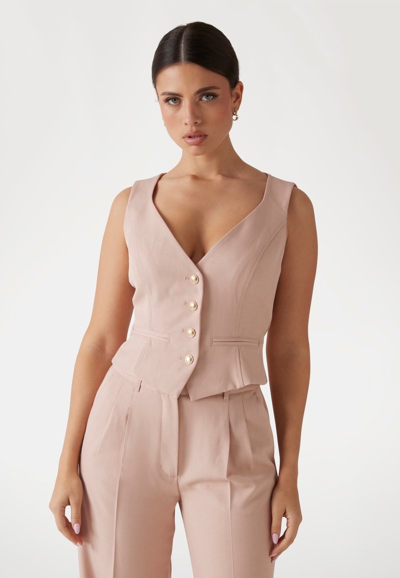 Blush-pink ärmellose Weste mit V-Ausschnitt, versehen mit fünf Perlenknöpfen und taillierter Passform, kombiniert mit passenden Hosen. Glatte Stofftextur.