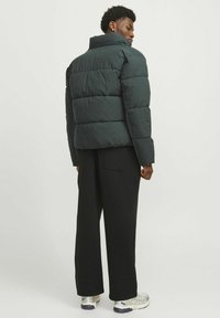 Gepolsterte schwarze Jacke mit hohem Kragen, gestepptem Design und lockerer Passform, kombiniert mit lockeren schwarzen Hosen und Sneakers in neutralen Farbtönen.