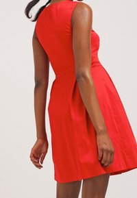 Rotes ärmelloses Kleid mit tailliertem Oberteil und weit ausgestellt Rock. Glatte Textur mit dezentem Glanz, die eine klassische A-Linie-Silhouette zeigt.