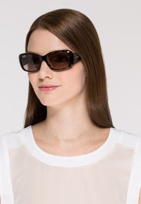 Ochelari de soare cu o ramă din broscuță țestoasă închisă și lentile maro cu gradienți. Textură netedă și formă rectangulară, cu branding subtil pe lateral.