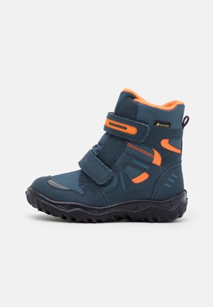 Botte d'hiver pour enfants bleu foncé et orange avec deux bandes Velcro, semelle texturée et étiquette Gore-Tex sur fond blanc.