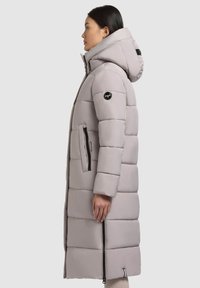 Svetlo siva pufferska jakna s kapuco, z debelimi horizontalnimi paneli, žepi na zadrgo in logotipom na rokavu. Gladka tekstura.