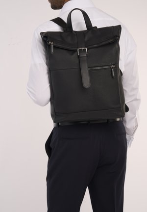 Schwarzer Rolltop-Rucksack mit strukturiertem Oberflächenmaterial, verstellbaren Trägern und vorderer Reißverschlusstasche. Beinhaltet eine Metall-Schnalle und Hardware-Akzente.