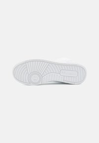 Sole di sneaker bianca con un materiale in gomma strutturato, caratterizzato da un palo di battistrada distintivo e un logo in rilievo.