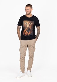 Camiseta negra con un gran gráfico de jirafa en el frontal, combinada con pantalones cargo beige y zapatillas blancas.