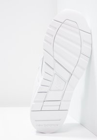 Bílá podešev tenisky New Balance s texturovanou gumou, obsahující horizontální drážky a kruhové vzory, označená názvem značky.