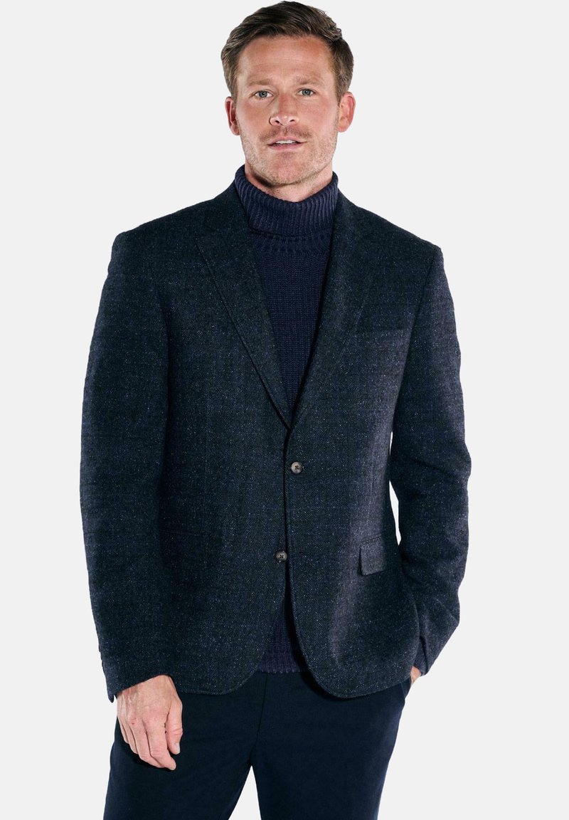 Marineblauer Wollblazer mit strukturiertem Stoff, einreihiges Design, zwei Fronttaschen und braunen Knöpfen. Trägt man über einem dunklen Rollkragenpullover.