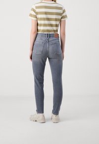 Grå jeans som sitter tight med fem fickor och en lätt urtvättning, tillsammans med en randig t-shirt i olivgrön och vit samt beige sneakers.