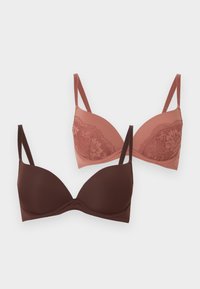 Δύο σουτιέν, ένα μονόχρωμο σκούρο καφέ και ένα σε χρώμα σκόνης ροζ με δαντελένιες λεπτομέρειες, και τα δύο με ρυθμιζόμενους ιμάντες σε λευκό φόντο.