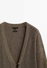 Gestrickte braune Strickjacke mit V-Ausschnitt, gerippter Struktur und einer einzelnen Knopfverschluss. Sichtbare Etiketten geben Stoffdetails und Herkunft an.