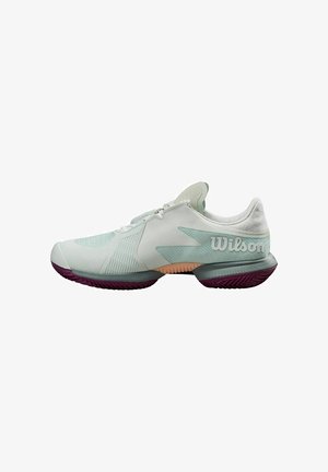 Baskets de tennis vert clair avec une tige texturée, accents blancs et semelle extérieure violette. Comprend une semelle rembourrée et une marque bien visible.