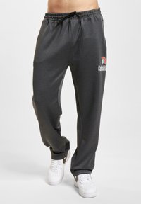 Grå joggebukser med elastisk midje og snor. Har en trykt logo på venstre lår. Glatt stofftekstur.