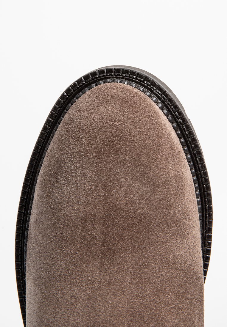 Brauner Wildlederschuh mit einer runden Zehenpartie, akzentuiert durch einen strukturierten schwarzen Lederbesatz entlang der Kante und einer glatten, matten Oberfläche.