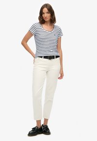 Marineblå og hvide stribede kortærmede T-shirt kombineret med cremefarvede jeans, fremhævet af et sort bælte og sorte sko med frynser.