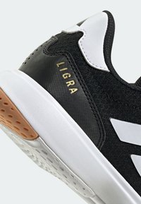 Gros plan d'une basket noire et blanche avec une semelle texturée et "LIGRA" imprimé en or sur le côté près du talon.