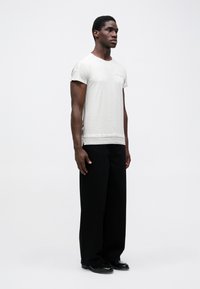 T-shirt leve de manga curta em cinza claro, com um corte descontraído, apresentando um logótipo discreto no peito e um tecido texturizado, combinado com calças largas pretas.