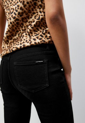 Jeans in denim nero con una forma aderente e tasche posteriori; abbinati a un top con stampa leopardata caratterizzato da una texture liscia e scollatura rotonda.