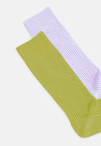 Ribbstickade strumpor i lavendel och olivgrönt. Varje strumpa har en enfärgad yta med en mjuk textur och en rektangulär tåform.
