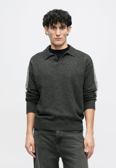 Charcoalgrijze gebreide trui met een polo kraag, geribde manchetten en een zoom. Bevat witte strepen langs de mouwen. Gekozen in combinatie met zwarte jeans.
