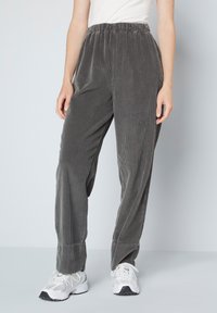 Grijze corduroy broek met een elastische tailleband, voorzien van een verticale ribbeltextuur en een losse pasvorm. Gepaard met witte sportschoenen.