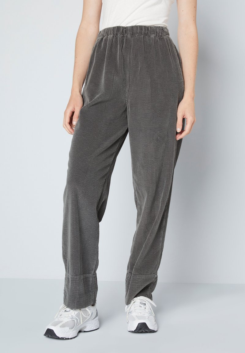 Grijze corduroy broek met een elastische tailleband, voorzien van een verticale ribbeltextuur en een losse pasvorm. Gepaard met witte sportschoenen.