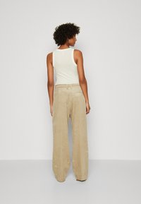 Lys beige ribbede cordfløyelsbukser med vide ben, kombinert med en tettsittende hvit tank topp som viser et enkelt design og myke teksturer.