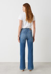 Blauwe high-waisted jeans met een flared leg ontwerp, met een achterzak en een bruin lederen label op de tailleband.