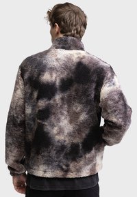Fleecejacke mit einem Batikmuster in Brauntönen, Grau und Creme. Sie hat einen hohen Kragen und eine weiche, strukturierte Oberfläche.