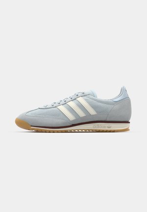 Sneaker in suede bluastro con tre strisce bianche, suola in gomma e tessuto a rete testurizzato. Presenta un copri punta liscio e un marchio sul tallone.
